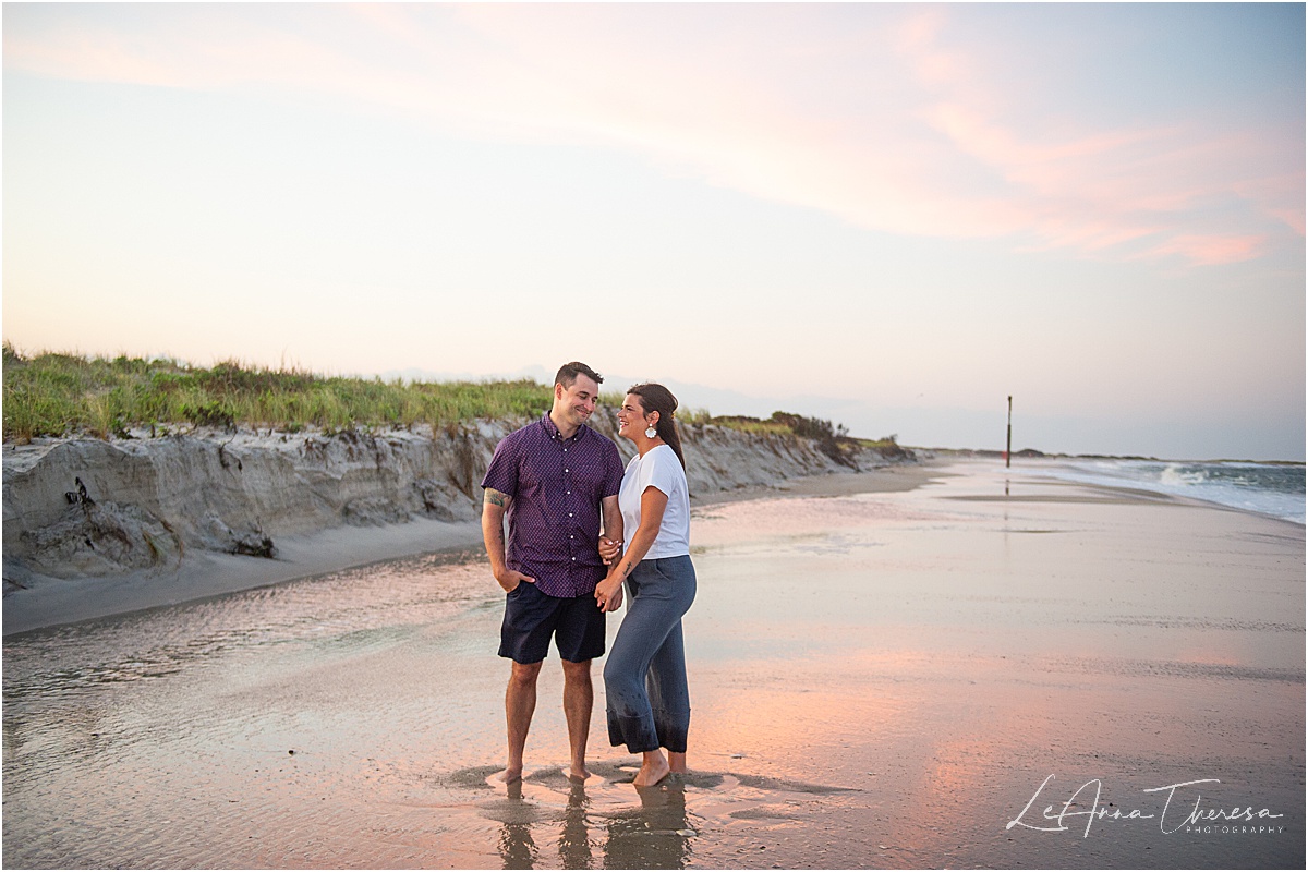 couple smiles at sunset at mast on beach in Barnegat light