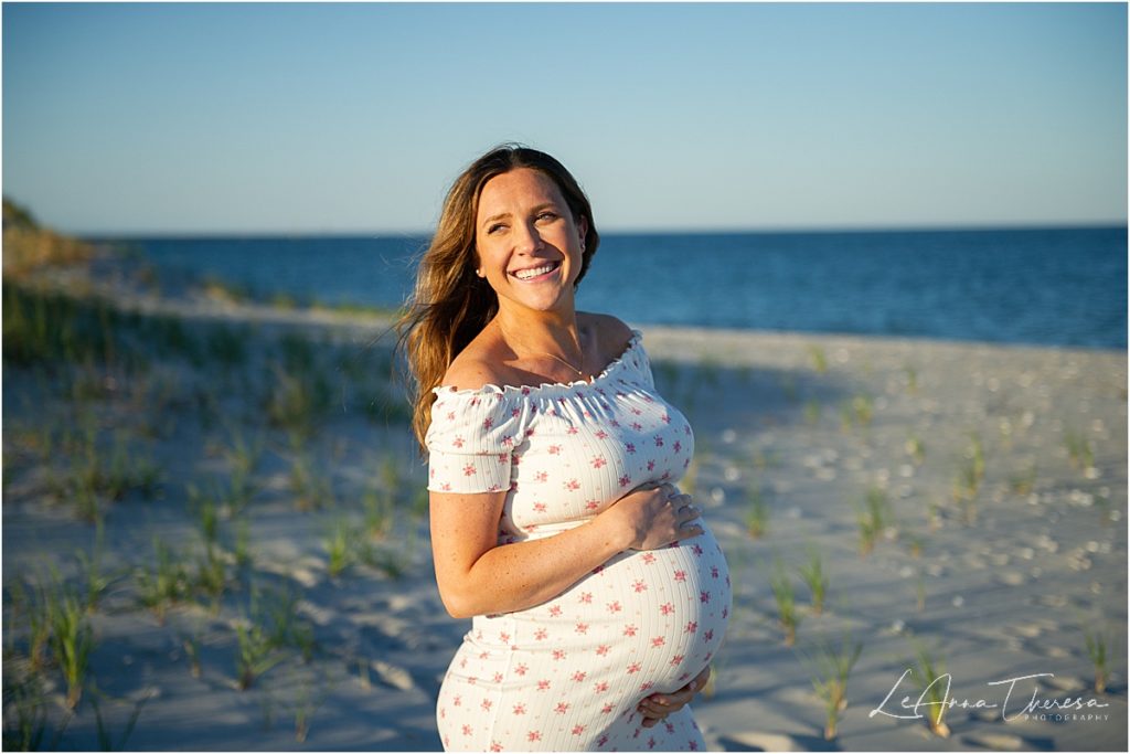 pregnant woman smiles on beach in front of ocean