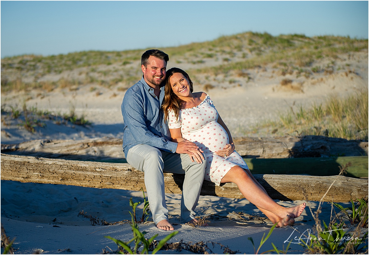 couple sits on driftwood for maternity photos on LBI