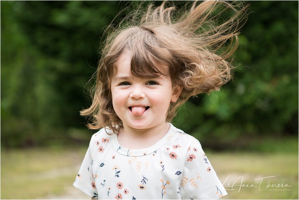 A smiling toddler girl sticking her tongue out and hair blowing wild in the wind